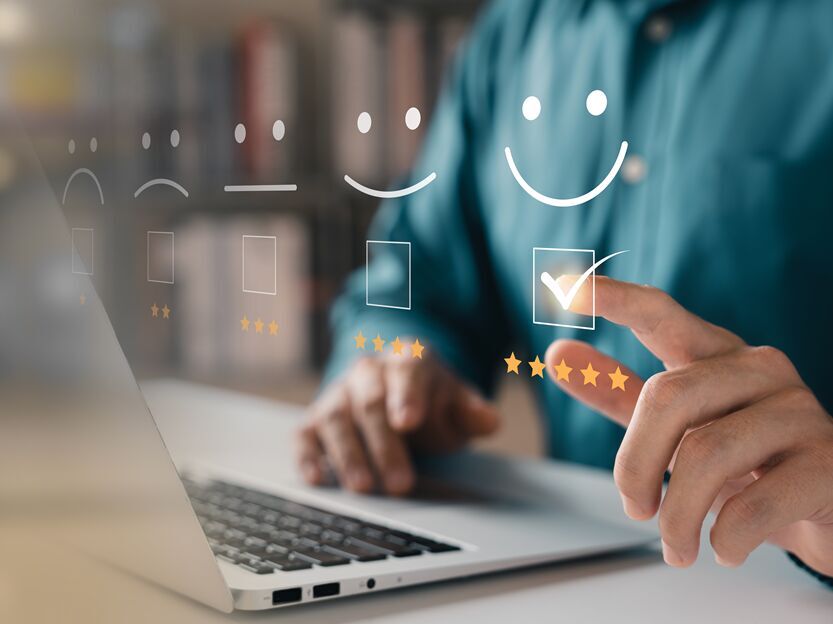 Symbolic image of customer satisfaction: a hand on a laptop gives a digital five-star rating with a smiley face.